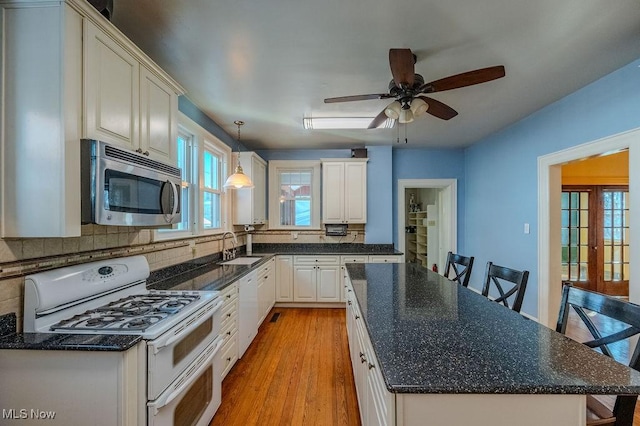 kitchen featuring white appliances, hanging light fixtures, light wood-type flooring, a kitchen bar, and sink