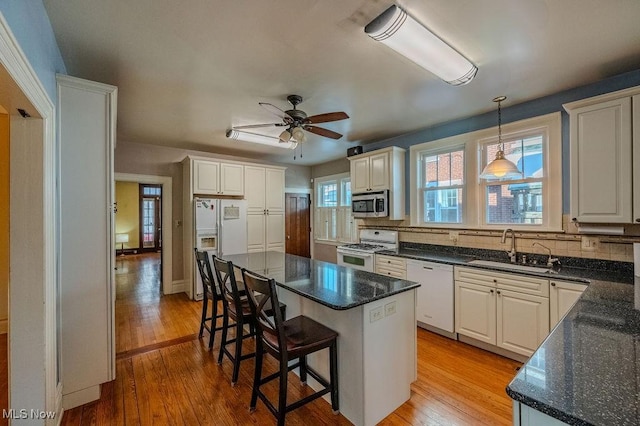 kitchen with white appliances, white cabinetry, a center island, and sink