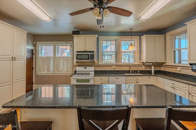 kitchen featuring sink, decorative light fixtures, white appliances, a kitchen bar, and dark stone counters