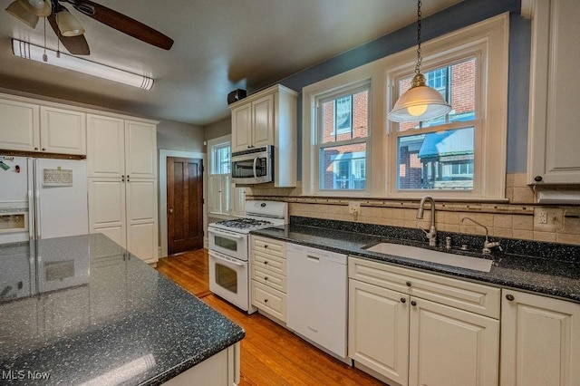 kitchen with white appliances, light hardwood / wood-style flooring, dark stone counters, ceiling fan, and sink