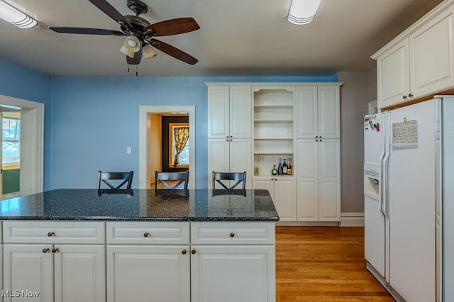 kitchen with white refrigerator with ice dispenser, a center island, a breakfast bar, white cabinets, and dark stone counters