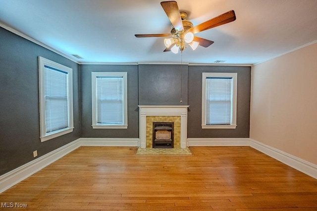 unfurnished living room with ceiling fan, light wood-type flooring, ornamental molding, and a tiled fireplace