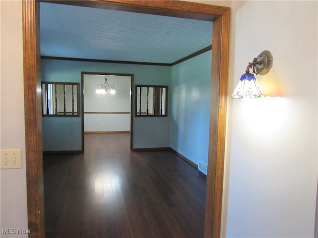 hallway with an inviting chandelier, dark wood-type flooring, ornamental molding, and a textured ceiling