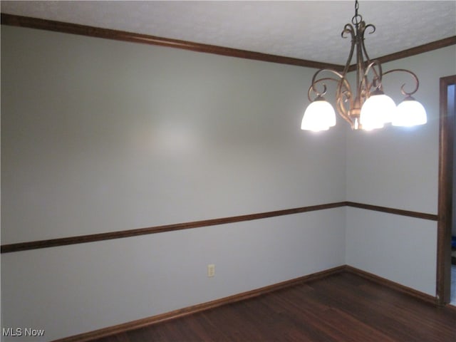 unfurnished room featuring dark wood-type flooring, ornamental molding, and an inviting chandelier