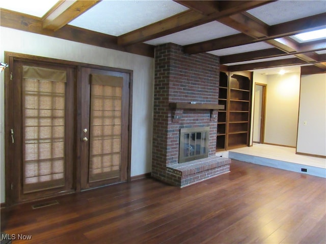 unfurnished living room featuring dark wood-type flooring, coffered ceiling, a brick fireplace, built in features, and beamed ceiling