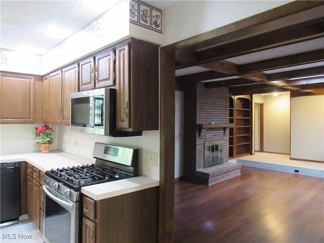 kitchen featuring dark brown cabinetry, a brick fireplace, dark hardwood / wood-style flooring, beamed ceiling, and stainless steel appliances