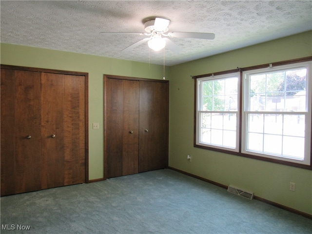 unfurnished bedroom featuring multiple closets, a textured ceiling, light colored carpet, and ceiling fan