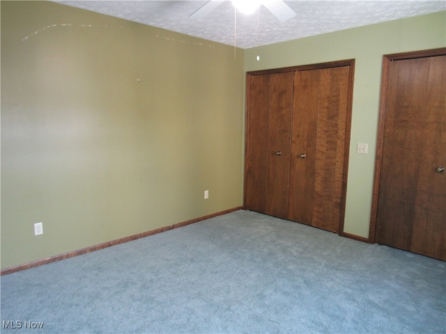 unfurnished bedroom with ceiling fan, light colored carpet, a textured ceiling, and two closets