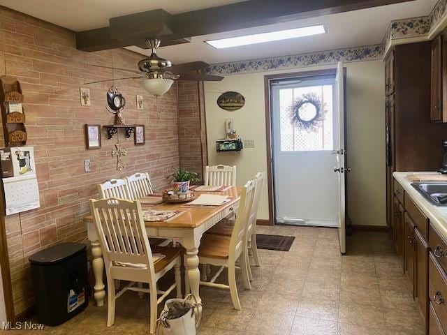 dining room with beamed ceiling, ceiling fan, brick wall, and sink