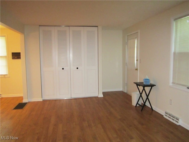 unfurnished bedroom with dark wood-type flooring, multiple windows, and a closet