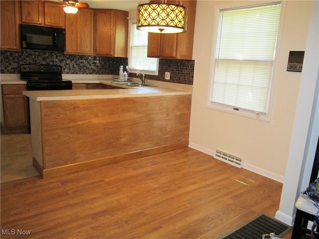 kitchen with pendant lighting, tasteful backsplash, black appliances, and kitchen peninsula