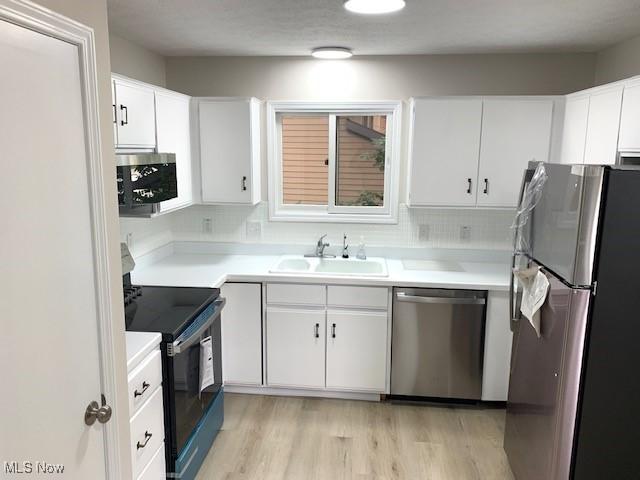 kitchen with appliances with stainless steel finishes, light hardwood / wood-style floors, white cabinetry, sink, and decorative backsplash