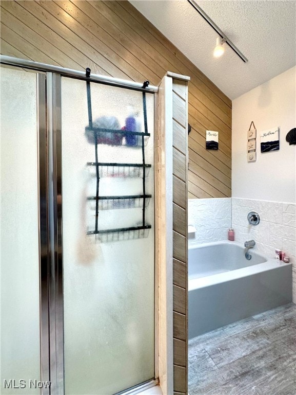 bathroom featuring hardwood / wood-style flooring, a textured ceiling, wooden walls, and separate shower and tub