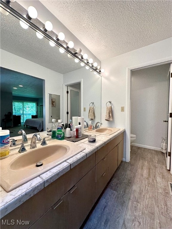 bathroom featuring double vanity, a textured ceiling, toilet, and hardwood / wood-style floors