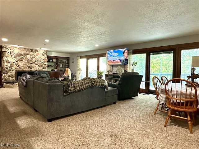 living room featuring a textured ceiling, a stone fireplace, plenty of natural light, and carpet