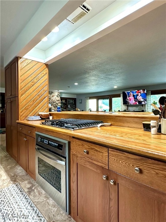 bar with light tile patterned floors, appliances with stainless steel finishes, a textured ceiling, and wooden counters