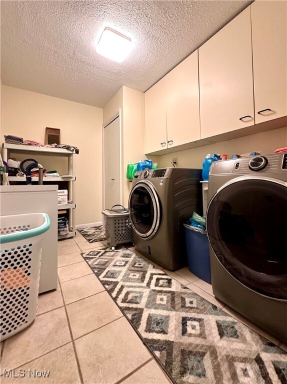 laundry area with washer and clothes dryer, light tile patterned flooring, a textured ceiling, and cabinets