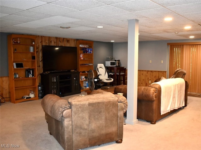 carpeted living room featuring wooden walls and a drop ceiling