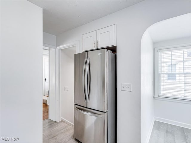 kitchen featuring arched walkways, baseboards, white cabinets, light wood-type flooring, and freestanding refrigerator