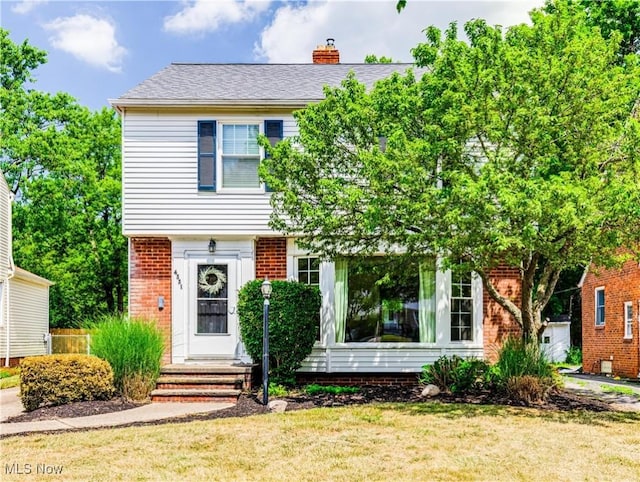 colonial house with brick siding, a chimney, and a front yard