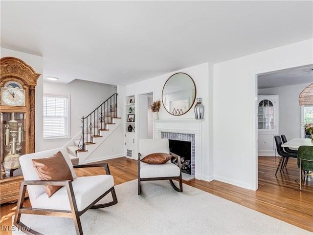 living area with wood finished floors, a brick fireplace, baseboards, and stairs