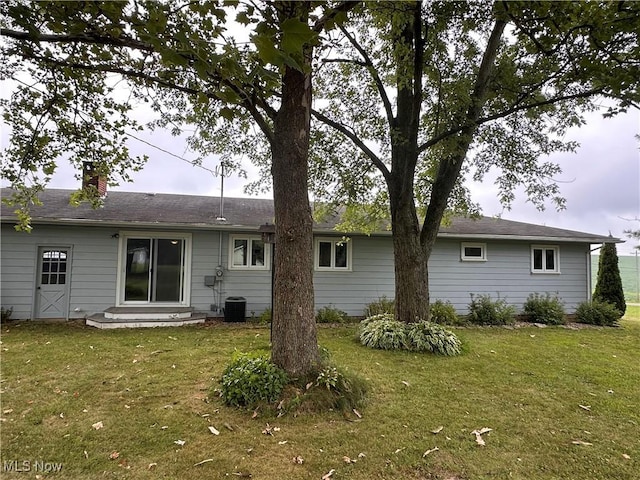 rear view of house with entry steps, a chimney, and a yard