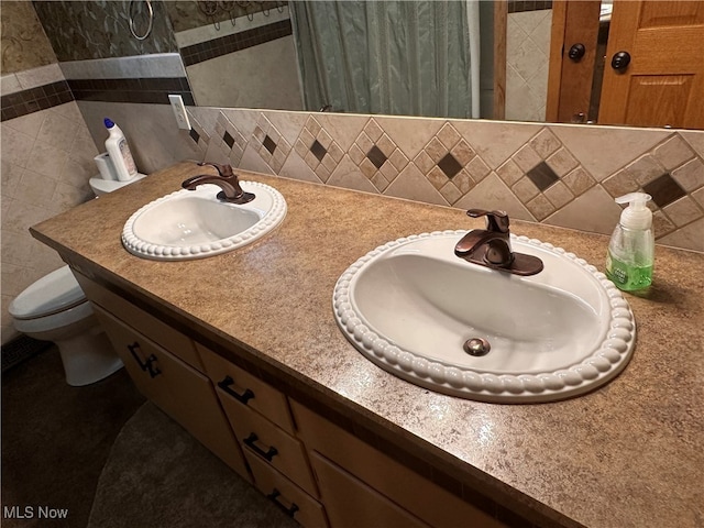 bathroom with dual vanity, toilet, and backsplash