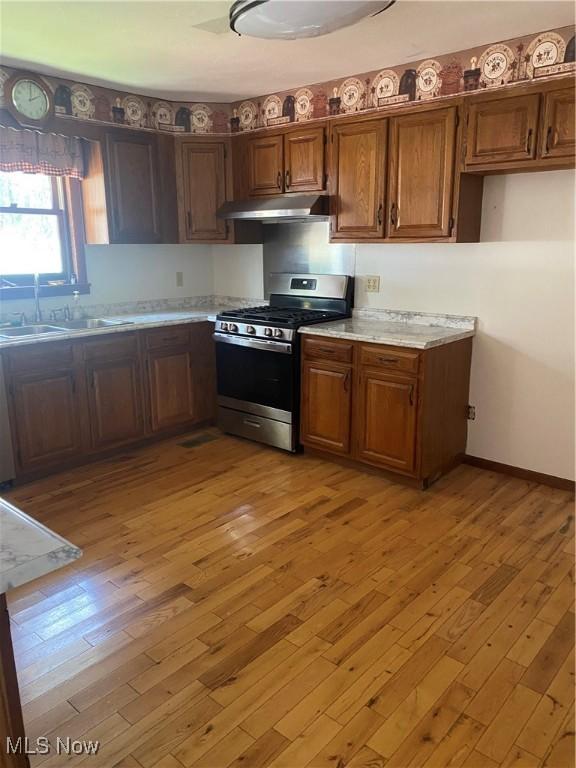 kitchen with light countertops, stainless steel range with gas stovetop, a sink, light wood-type flooring, and under cabinet range hood