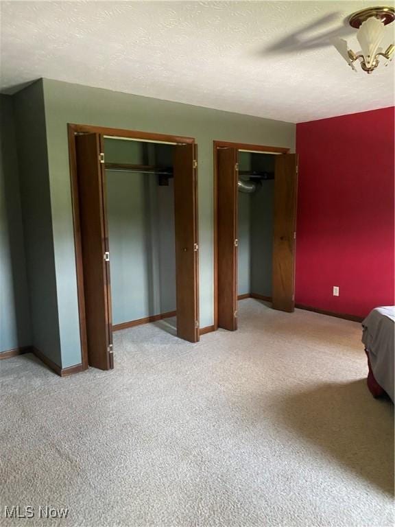 unfurnished bedroom featuring a textured ceiling, light colored carpet, a ceiling fan, baseboards, and multiple closets