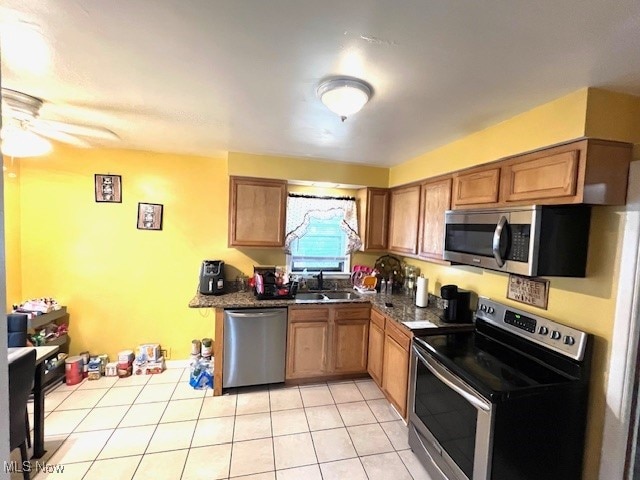 kitchen with ceiling fan, stainless steel appliances, sink, dark stone countertops, and light tile patterned floors