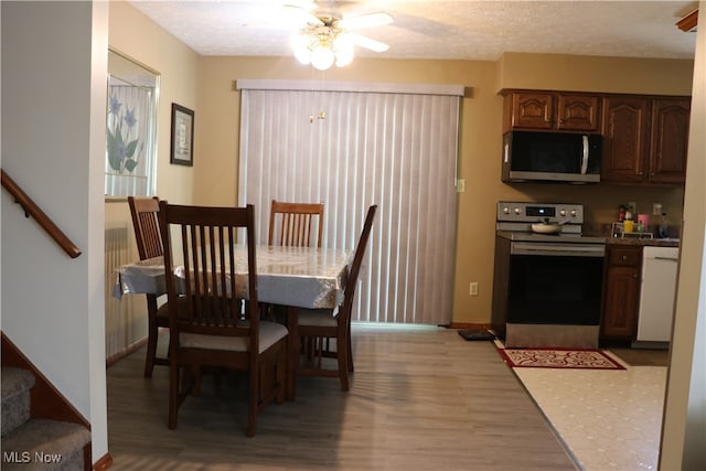 dining area with a textured ceiling, ceiling fan, and light wood-type flooring