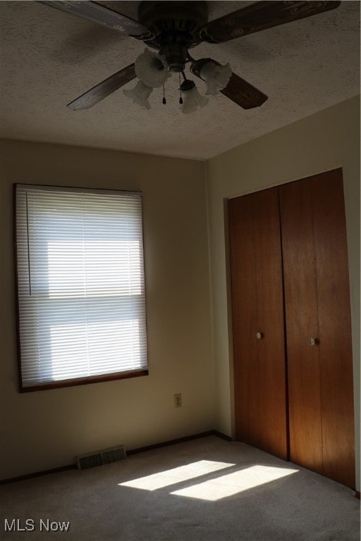 unfurnished bedroom with a textured ceiling, carpet, a closet, and ceiling fan