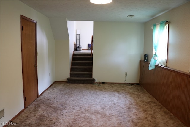 stairway with a textured ceiling and light colored carpet