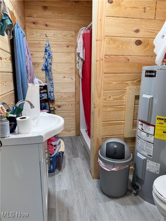 bathroom featuring hardwood / wood-style floors, wood walls, toilet, electric water heater, and a shower with curtain