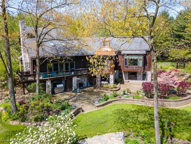 rear view of house featuring a patio, a wooden deck, a chimney, stone siding, and a lawn