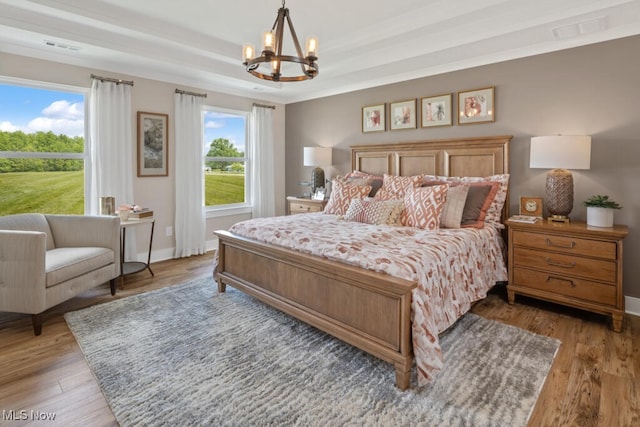 bedroom featuring a raised ceiling, an inviting chandelier, and hardwood / wood-style flooring