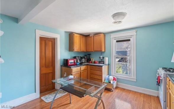 kitchen with baseboards, light wood finished floors, brown cabinetry, and white range with gas stovetop