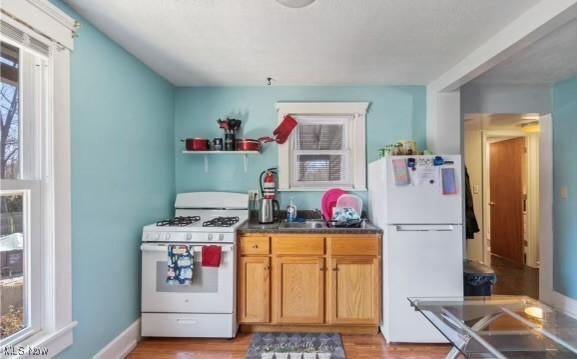 kitchen featuring light wood-type flooring, dark countertops, white appliances, and baseboards