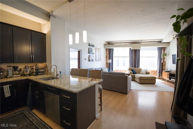 kitchen with decorative light fixtures, stainless steel dishwasher, open floor plan, a sink, and a peninsula