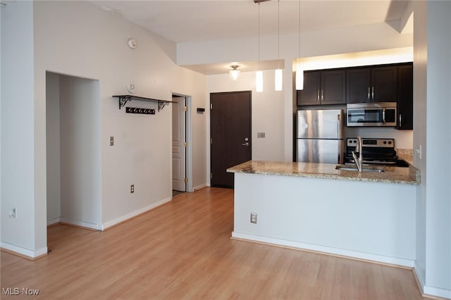 kitchen featuring light stone counters, a peninsula, appliances with stainless steel finishes, light wood finished floors, and decorative light fixtures