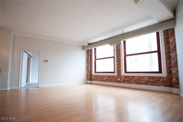 unfurnished room with brick wall, light wood-type flooring, and baseboards