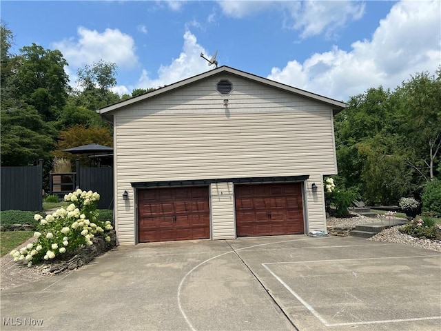 garage with concrete driveway and fence