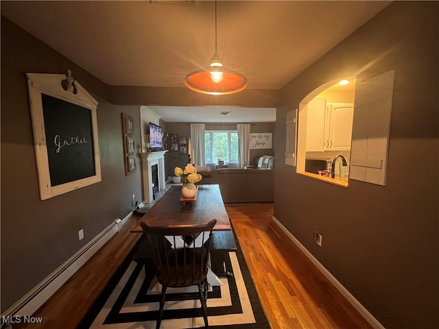 dining area with a baseboard radiator, a fireplace, baseboards, and wood finished floors