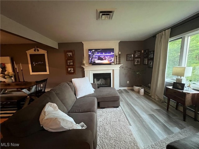 living area with a baseboard heating unit, a fireplace, baseboards, and wood finished floors