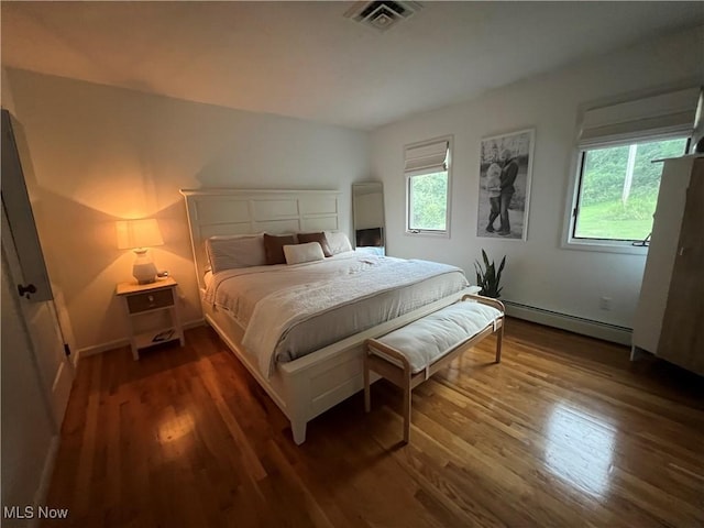 bedroom featuring a baseboard heating unit, wood finished floors, visible vents, and multiple windows