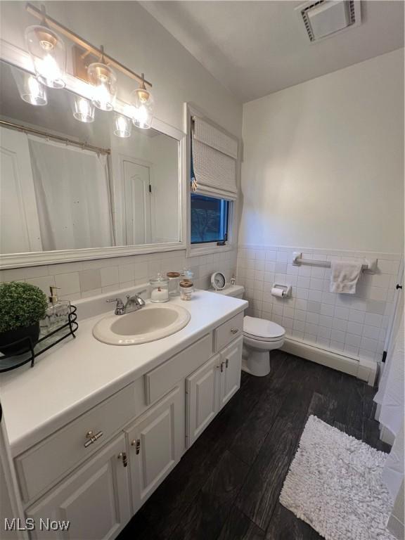 full bath with a wainscoted wall, tile walls, visible vents, vanity, and wood finished floors