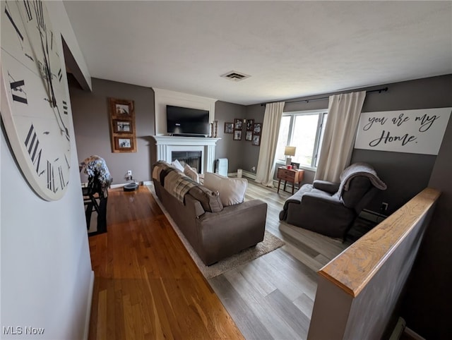 living room featuring a fireplace, wood finished floors, visible vents, and baseboards