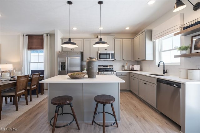 kitchen featuring light wood-type flooring, gray cabinets, a sink, stainless steel appliances, and decorative backsplash