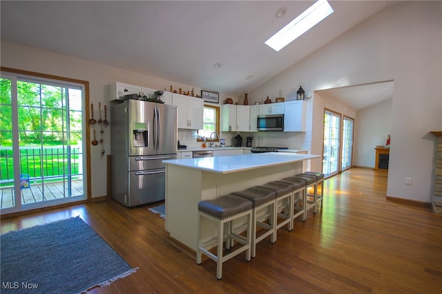 kitchen with appliances with stainless steel finishes, white cabinets, hardwood / wood-style floors, backsplash, and a skylight