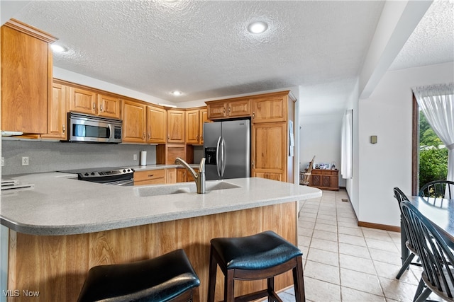 kitchen with light tile patterned floors, kitchen peninsula, a kitchen bar, stainless steel appliances, and sink